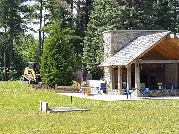 Stone fireplace and timber pavilion beside the lawn and trees at Base Camp